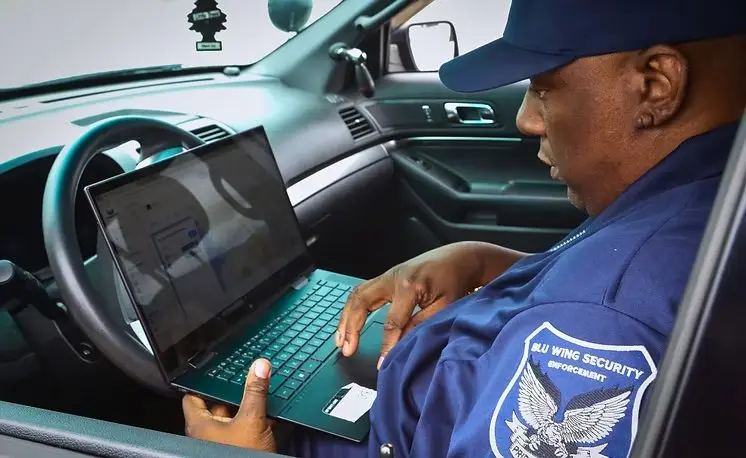 Blu Wing guard writing a report on a laptop in a patrol vehicle